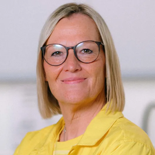 Zu sehen ist Corinna van Suntum, Vorstandsmitglied der IKEA Stiftung. Sie hat blonde halblange glatte Haare, trägt eine Brille und eine sonnengelbe Bluse, der Hintergrund ist hell und unscharf gehalten.
