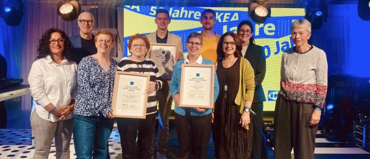 Gruppenfoto der Preisträgerinnen und Preisträger des Preises der IKEA Stiftung 2024: Mehrere Personen stehen auf einer Bühne und halten gerahmte Urkunden der IKEA Stiftung, im Hintergrund eine beleuchtete Veranstaltungswand.