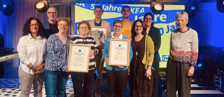 Gruppenfoto der Preisträgerinnen und Preisträger des Preises der IKEA Stiftung 2024: Mehrere Personen stehen auf einer Bühne und halten gerahmte Urkunden der IKEA Stiftung, im Hintergrund eine beleuchtete Veranstaltungswand.